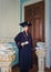 Student mannequin, inside a library, dressed as a graduate with a black academic cap and gown, holding a diploma in hand.