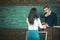 Student and professor having discussion in classroom. Rear view girl in blue jeans and white jumper standing in front of