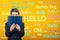 Student woman holding a textbook over yellow wall written with word hello translated in different languages. Opportunity for