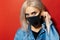 Studio close-up portrait of young blonde girl with blue eyes, wearing respiratory face mask of black color, against coronavirus.