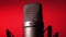 Studio condenser microphone rotates on red background.