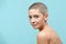 Studio headshot portrait of a beautiful young caucasian woman with shaved head against pastel blue background. Cancer survivor.