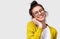 Studio horizontal close up portrait of candid smiling woman in eyeglasses touching earphones.