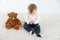 Studio photo with aerial white background of a baby sitting with a teddy bear
