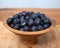 A studio photograph of a bowl of blueberries in a small wooden bowl