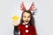Studio portrait of happy teenage girl holding a yellow star in hand, wearing red reindeer horns and Santa Claus costume on white.