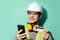 Studio portrait of happy young builder man, engineer, paying online with smartphone and credit card.