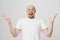 Studio portrait of overwhelmed and excited bald caucasian man with beard shouting of happiness and spreading hands