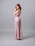 Studio portrait of pensive ginger glamour young woman in pink asymmetrical dress on grey background. Bridesmaid`s look.