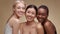 Studio portrait of three happy multiethnic ladies laughing to camera, enjoying friendship, hugging over beige background