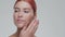 Studio portrait of young, beautiful and natural redhead woman applying skin care cream. Face lifting, cosmetics and make