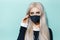 Studio portrait of young blonde girl wearing black respiratory face mask against coronavirus on aqua menthe color.