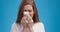 Studio portrait of young sick lady blowing her nose, blue background, slow motion