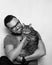 Studio portrait of a young smiling man with a beard and glasses holding a tabby cat in his arms. Grey background. White background