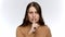 Studio portrait of young woman holding finger at mouth and saying shhh. Concept of keeping secret and silence