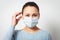 Studio portrait of young woman wearing a face mask, looking at camera, close up, isolated on gray background. Flu epidemic, dust