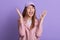 Studio shot of adorable girl screaming happily while posing indoor against lilac wall with palms up, lady wearing rose leather