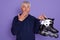 Studio shot of astonished white haired senior man with roller skates in hands, being shocked, posing with big eyes, covering his