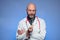 Studio shot of a bald doctor with beard in his 40s, holding syringe in his hand, blue background. Vaccination and health care