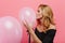 Studio shot of blissful woman with blonde hair kissing pink balloon. Indoor portrait of chilling young lady in black