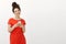 Studio shot of bright charming curly-haired female in cute red dress smiling broadly and tilting head while holding