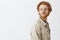 Studio shot of dreamy handsome young redhead guy passing by interesting store and turning left with calm expression