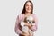 Studio shot of European woman with satisfied expression, holds pedigree puppy, enjoys loyalty of four legged friend, carries dog