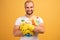 Studio shot of good looking pleased man with bald head, hugs cleaning detergents, wears t shirt, isolated over yellow background