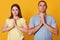 Studio shot of grateful thankful young couple holding hands in praying gesture, sincere love, man and woman directly at camera,