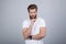 Studio shot of handsome pensive male holds chin, thinks about something, dressed in white t-shirt, stands against white background