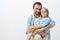 Studio shot of happy positive father and son with vitiligo, hugging and smiling broadly at camera, being pleased and