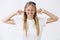 Studio shot of intense good-looking young girl with fair hair in headband grimcaing, clenching teeth closing ears and