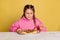 Studio shot of little cute girl sitting and tasting delicious Italian pizza isolated on yellow studio background.