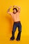 Studio shot of mature friendly bearded hairy man, hippie in stylish sunglasses and flared jeans dancing over yellow