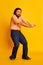 Studio shot of mature friendly bearded hairy man, hippie in stylish sunglasses and flared jeans dancing over yellow