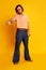 Studio shot of mature friendly bearded hairy man, hippie in stylish sunglasses and flared jeans posing over yellow