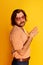 Studio shot of mature friendly bearded hairy man, hippie in stylish sunglasses and flared jeans posing over yellow