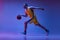 Studio shot of muscled man, basketball player training with ball isolated on purple background in neon light. Goals