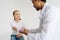 Studio shot of positive pediatrician male doctor in uniform consulting smiling little girl patient with broken hand