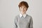 Studio shot of pretty slender redhead woman with freckles, standing in sweater over white shirt against gray background