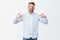 Studio shot of self-assured proud redhead male entrepreneur in shirt over t-shirt pointing at himself and staring with