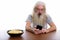 Studio shot of senior bearded man using mobile phone with bowl o