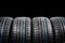 Studio shot of a set of summer car tires on black background. Tire stack background. Car tyre protector close up. Black rubber tir