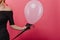 Studio shot of slim white woman holding helium pink balloon. Party photo of graceful female model in black dress posing