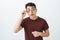 Studio shot of smart curious handsome man in round glasses and red t-shirt, raising eyebrows with interest and holding