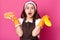 Studio shot of surprised female housekeeper holds sponge and detergent spray in hands, having much work to do, uses cleanser,