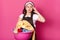 Studio shot of tired housewife with headache, wears brown apron and casual white t shirt, poses against pink studio wall, keeps