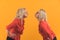 Studio shot on yellow background of two cute millenial blonde women standing apart and giving kisses to each other from