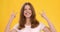 Studio shot of young cheerful woman showing punk horn gesture, orange background, slow motion