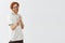 Studio shot of young funny and slim caucasian redhead guy with beard in geek glasses making finger fun gestures and